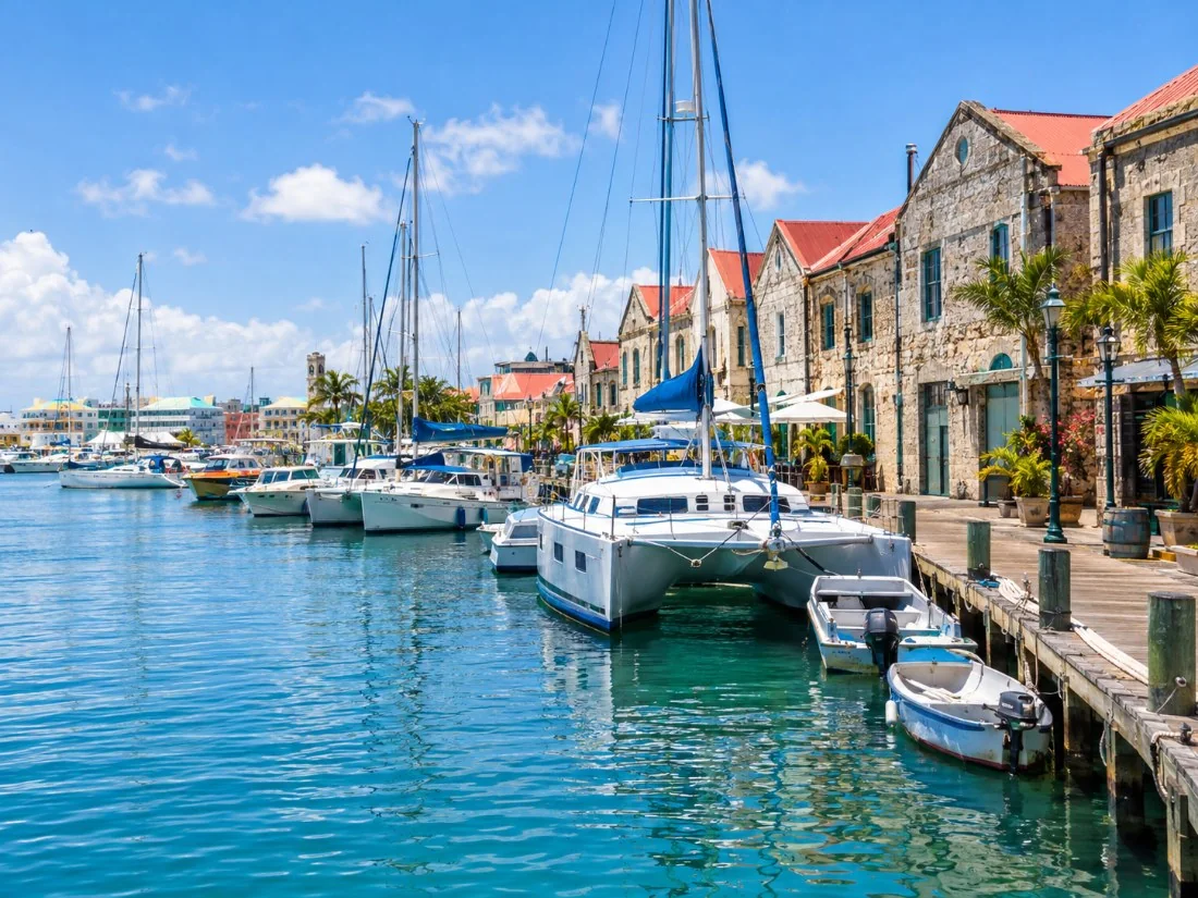 Catamarans and small boats moored along the Careenage in Bridgetown beside old stone warehouses